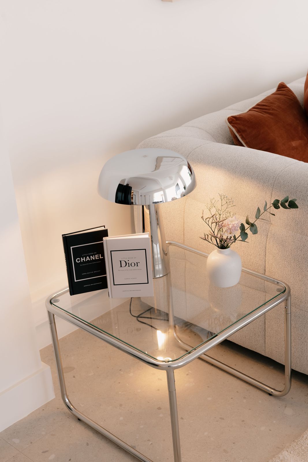 Glazen bijzettafel met chromen lamp, boeken en bloemetjes