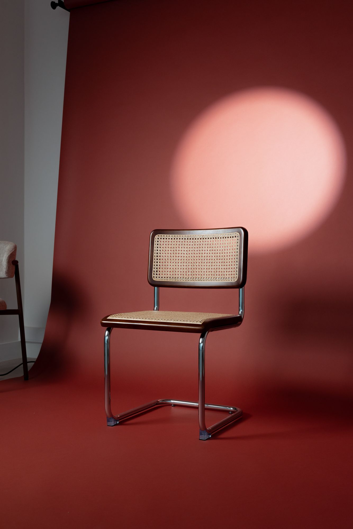 Stoel met rieten zitting voor een rode backdrop met roze spotlicht